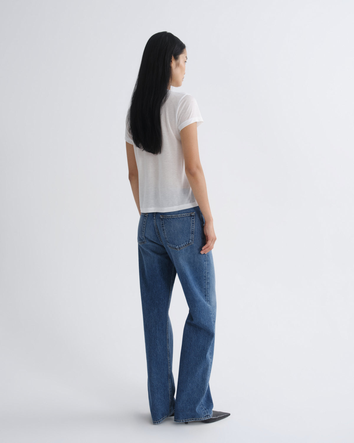 Person wearing blue jeans and a white shirt on a plain background