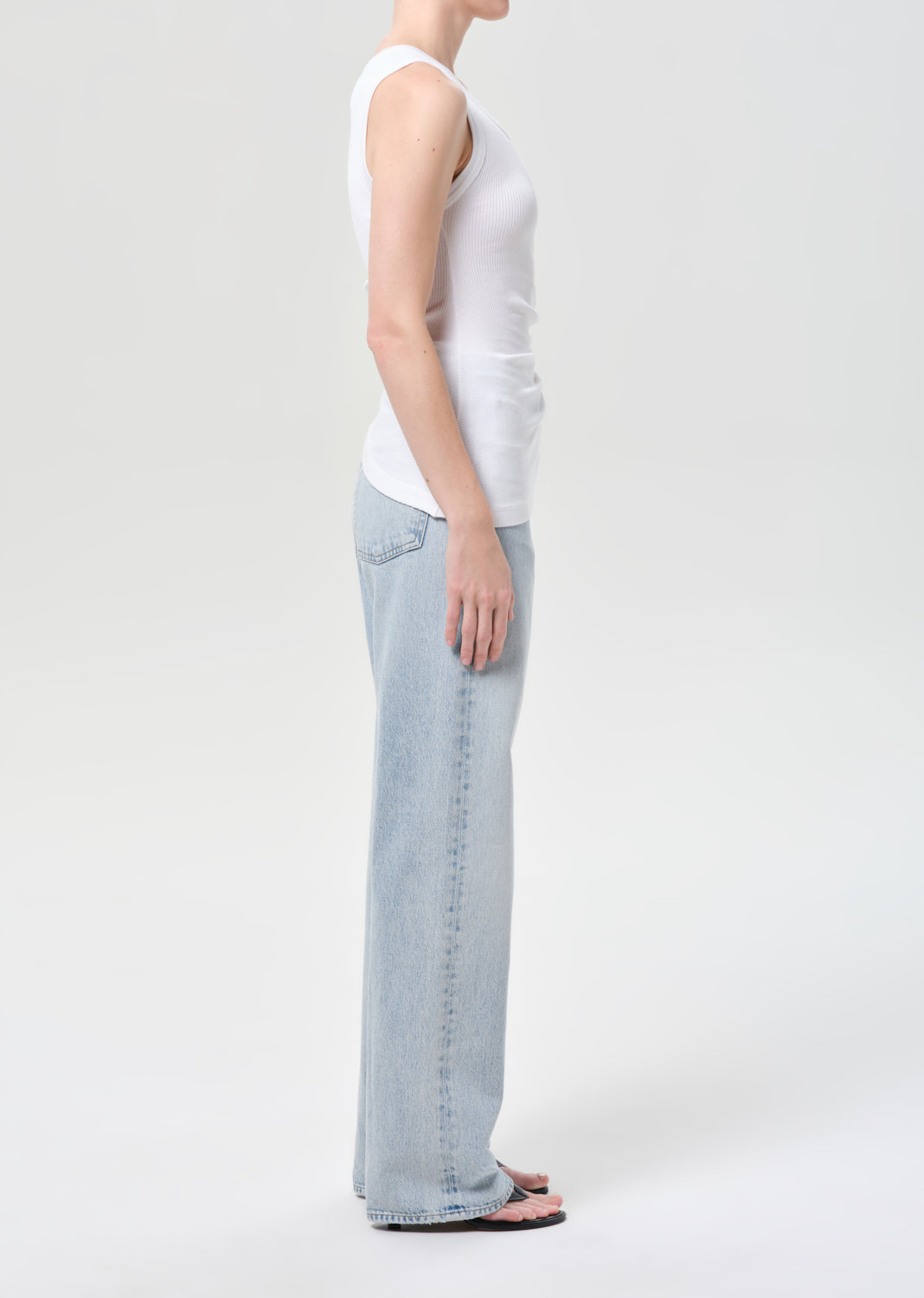Person wearing a white tank top and light blue jeans on a plain background