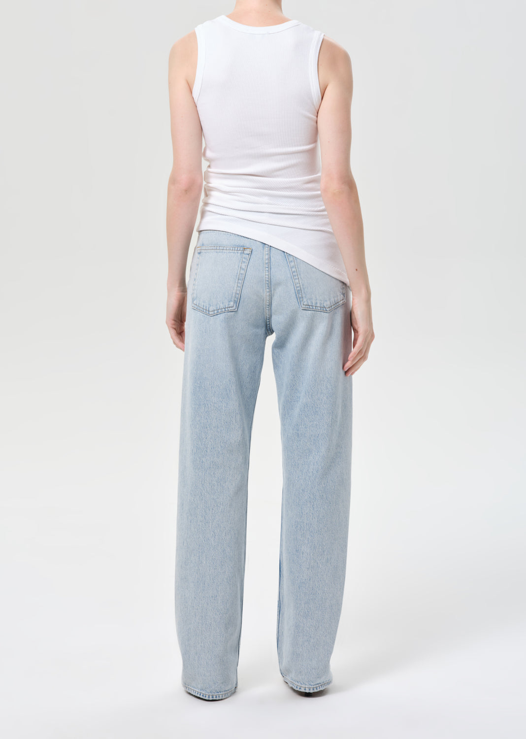 Person wearing a white sleeveless top and light blue jeans on a white background