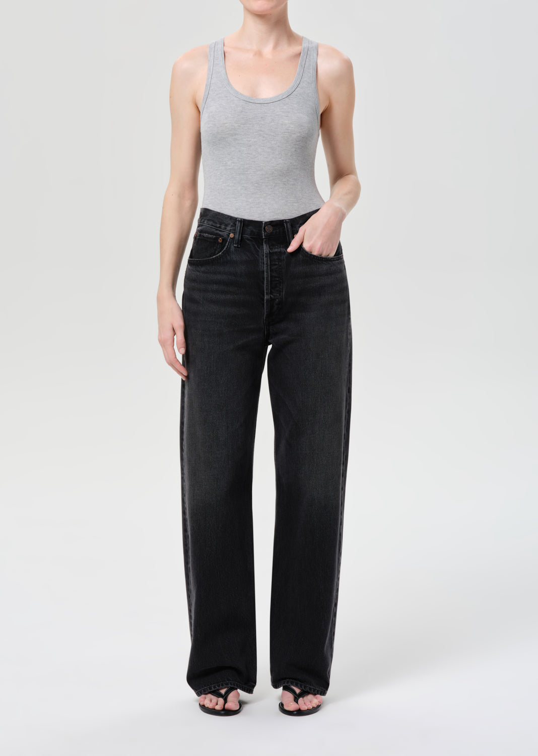 Person wearing a gray tank top and black wide-leg jeans on a white background