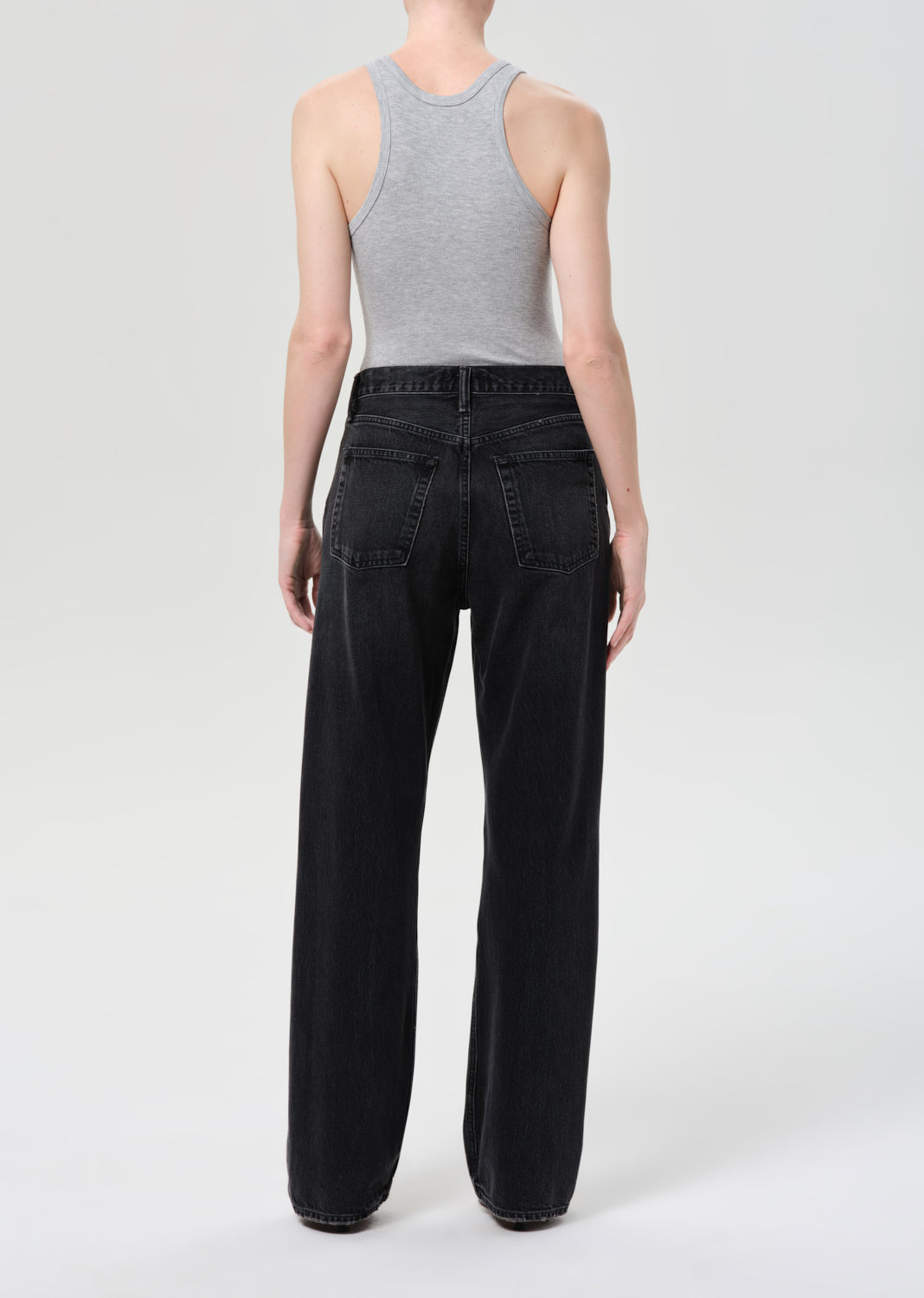 Person wearing a gray tank top and black wide-leg jeans on a white background