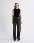 A model stands against a plain light gray studio background wearing a sleeveless black ribbed top and dark gray wide-leg jeans.