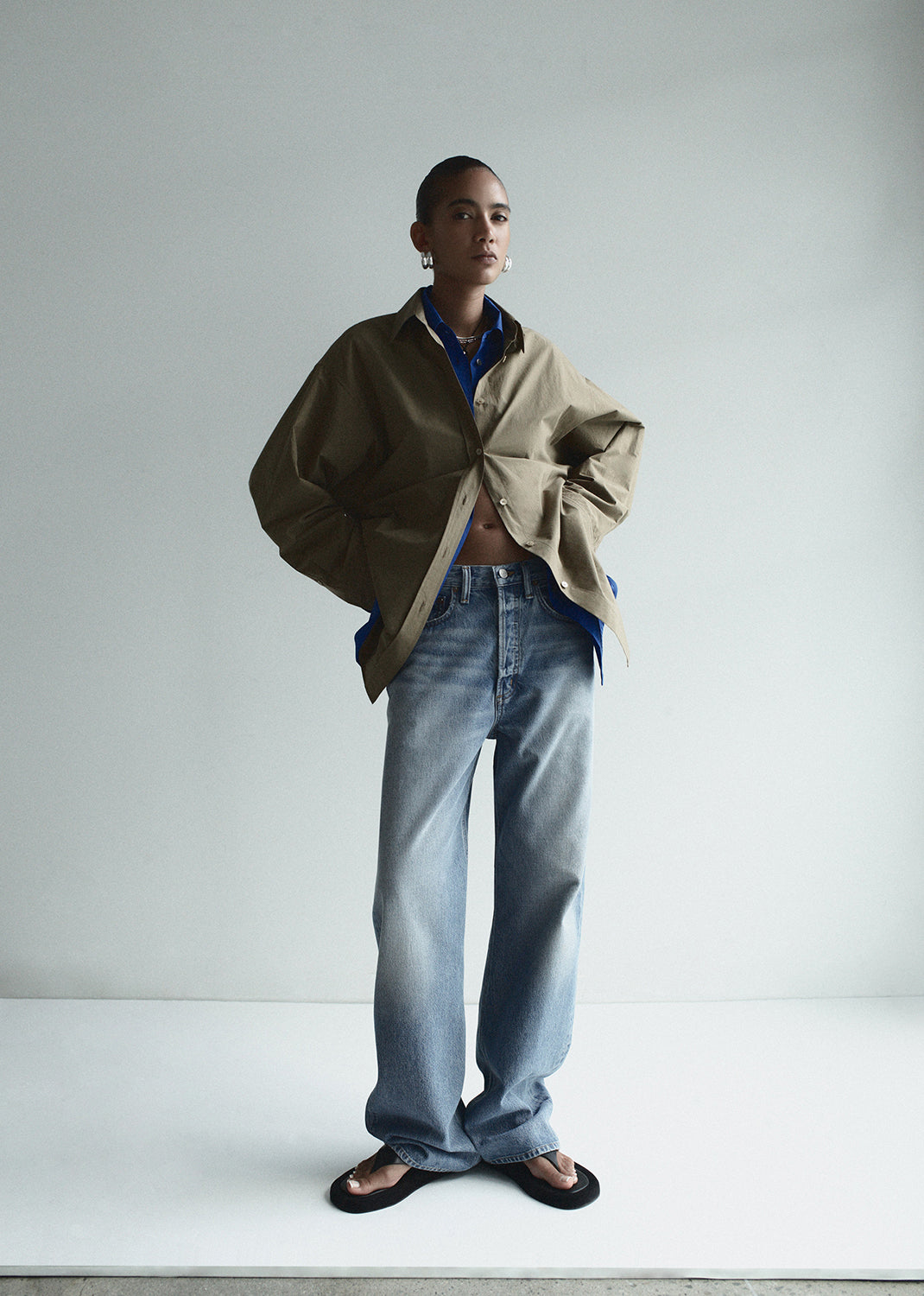 Person wearing a beige coat over a blue shirt and jeans on a white background