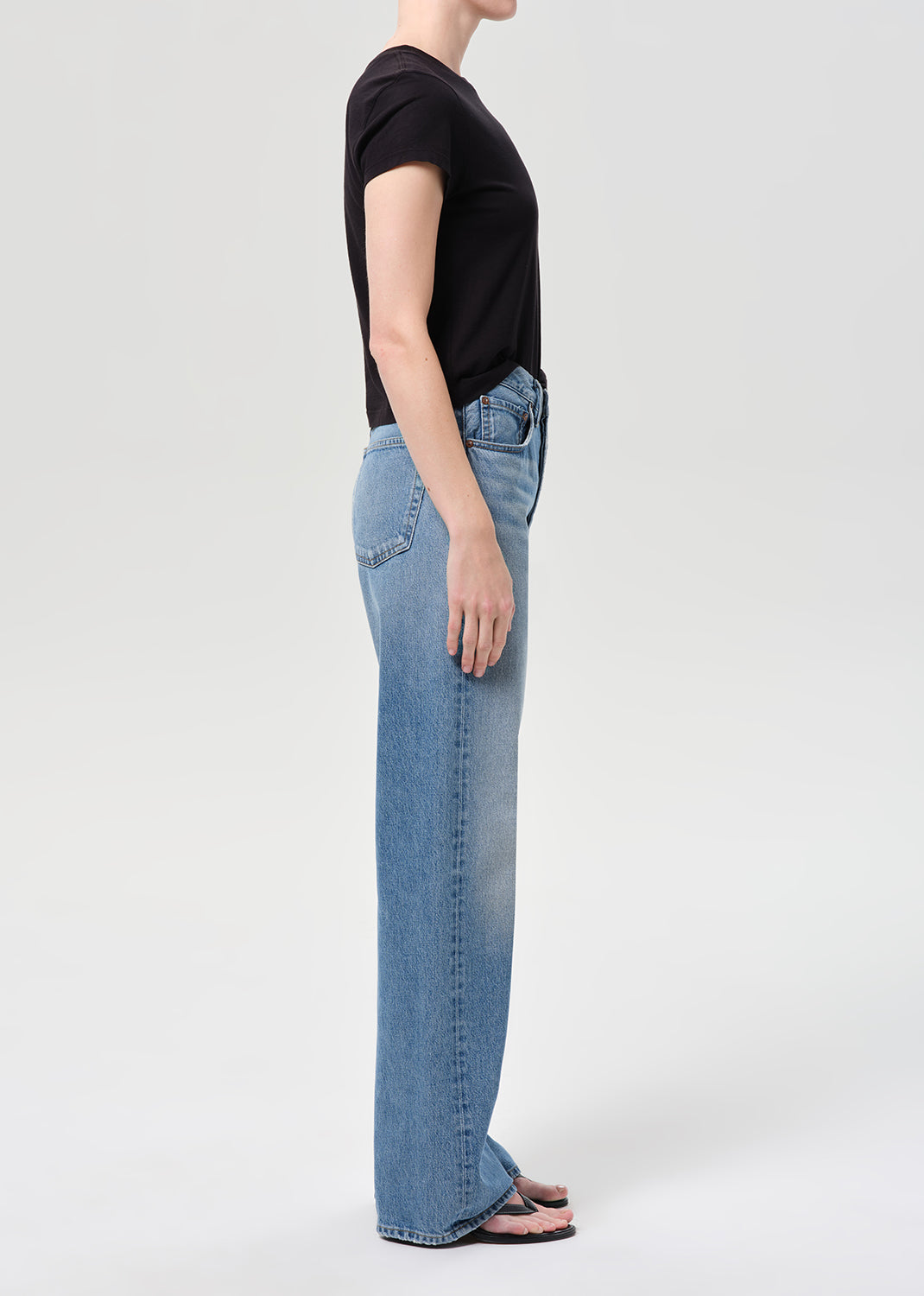 Person wearing blue jeans and a black top on a white background