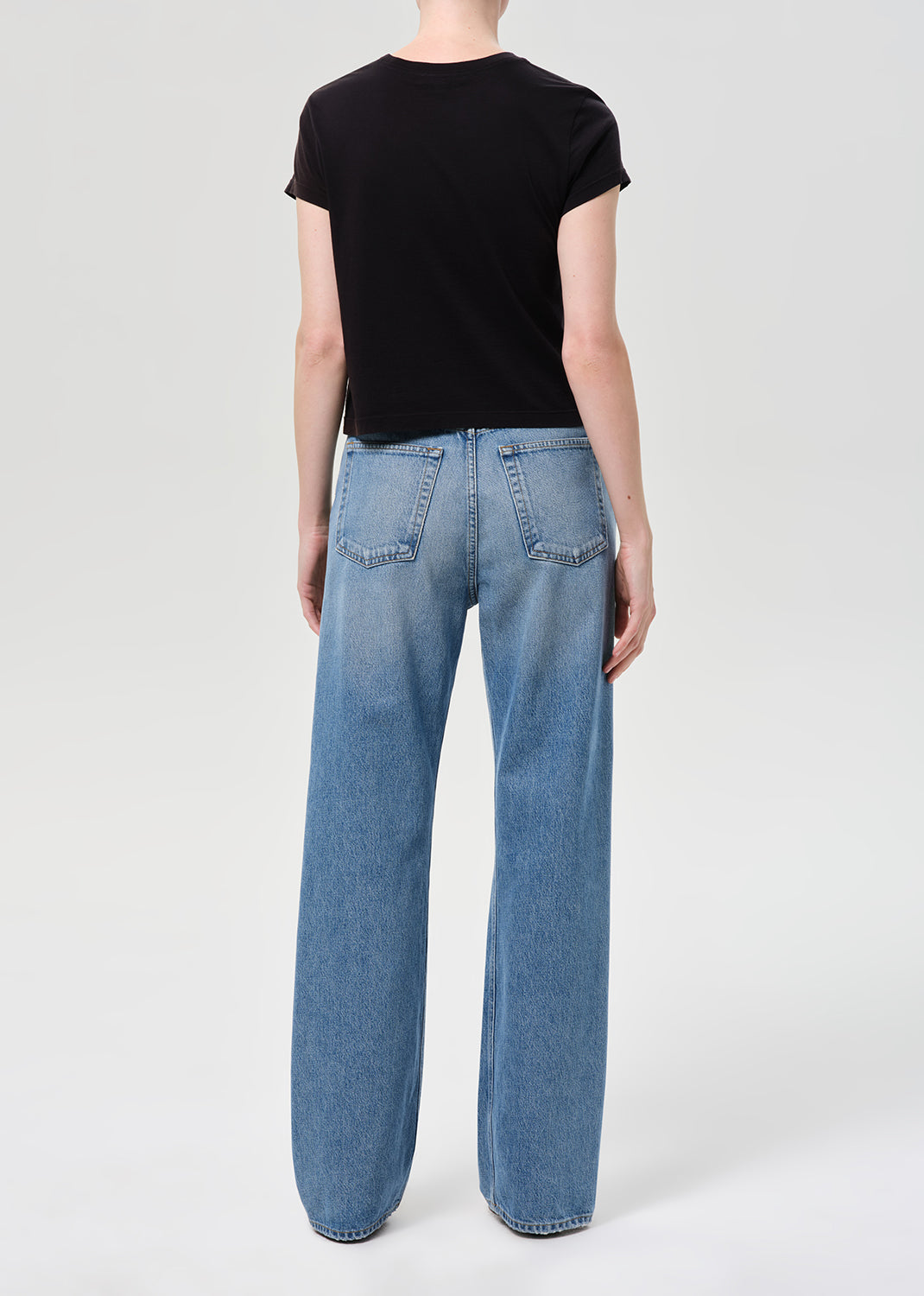 Person wearing blue jeans and a black t-shirt on a white background