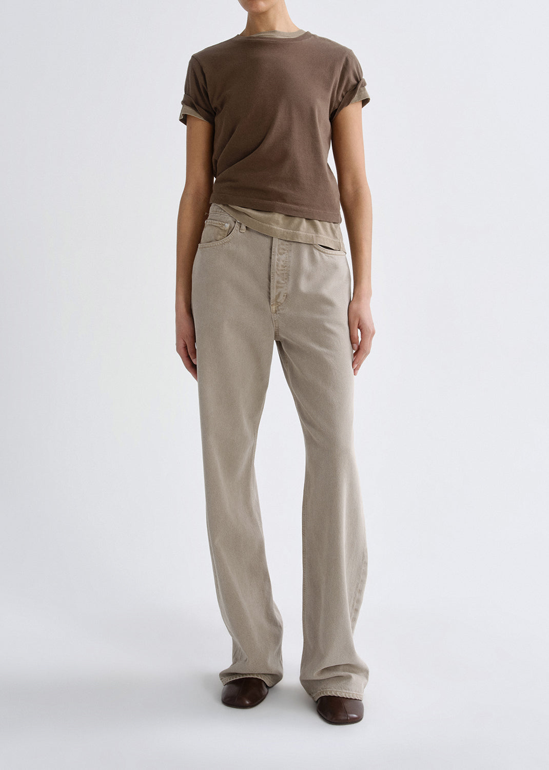 Person wearing a brown t-shirt and beige pants on a grey background