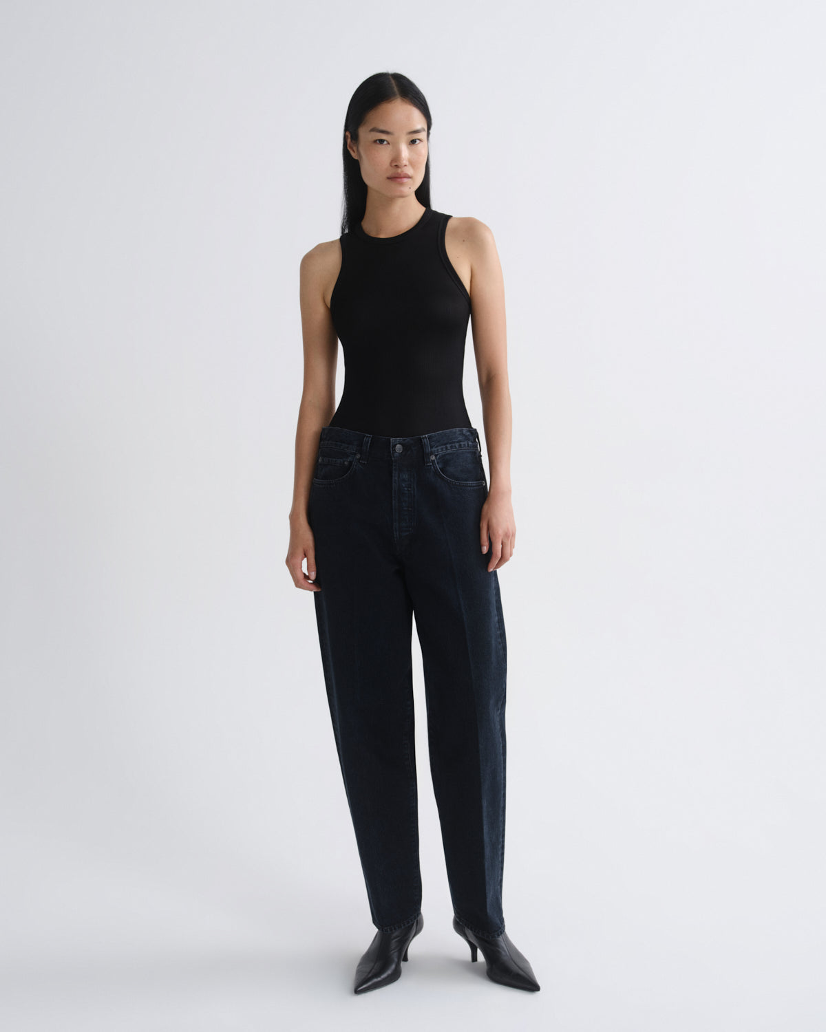 Woman wearing a black sleeveless top and dark jeans on a white background