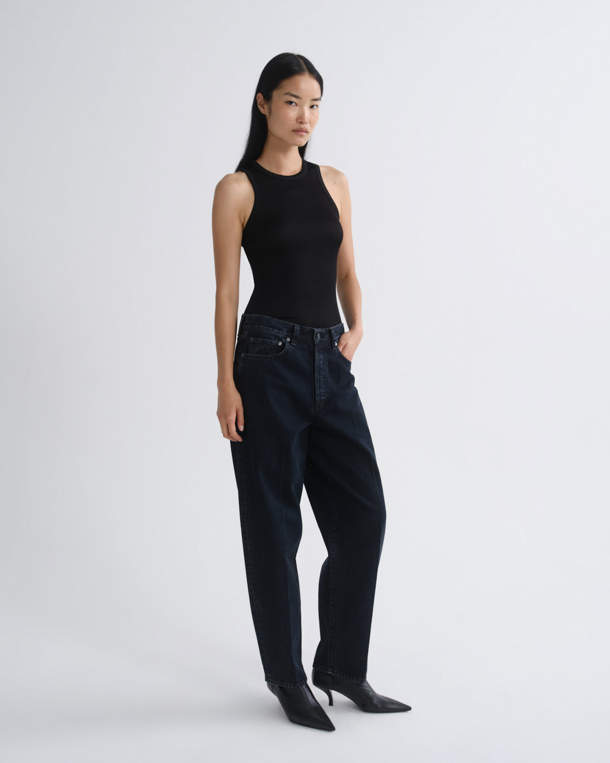 Woman wearing a black sleeveless top and dark jeans on a white background