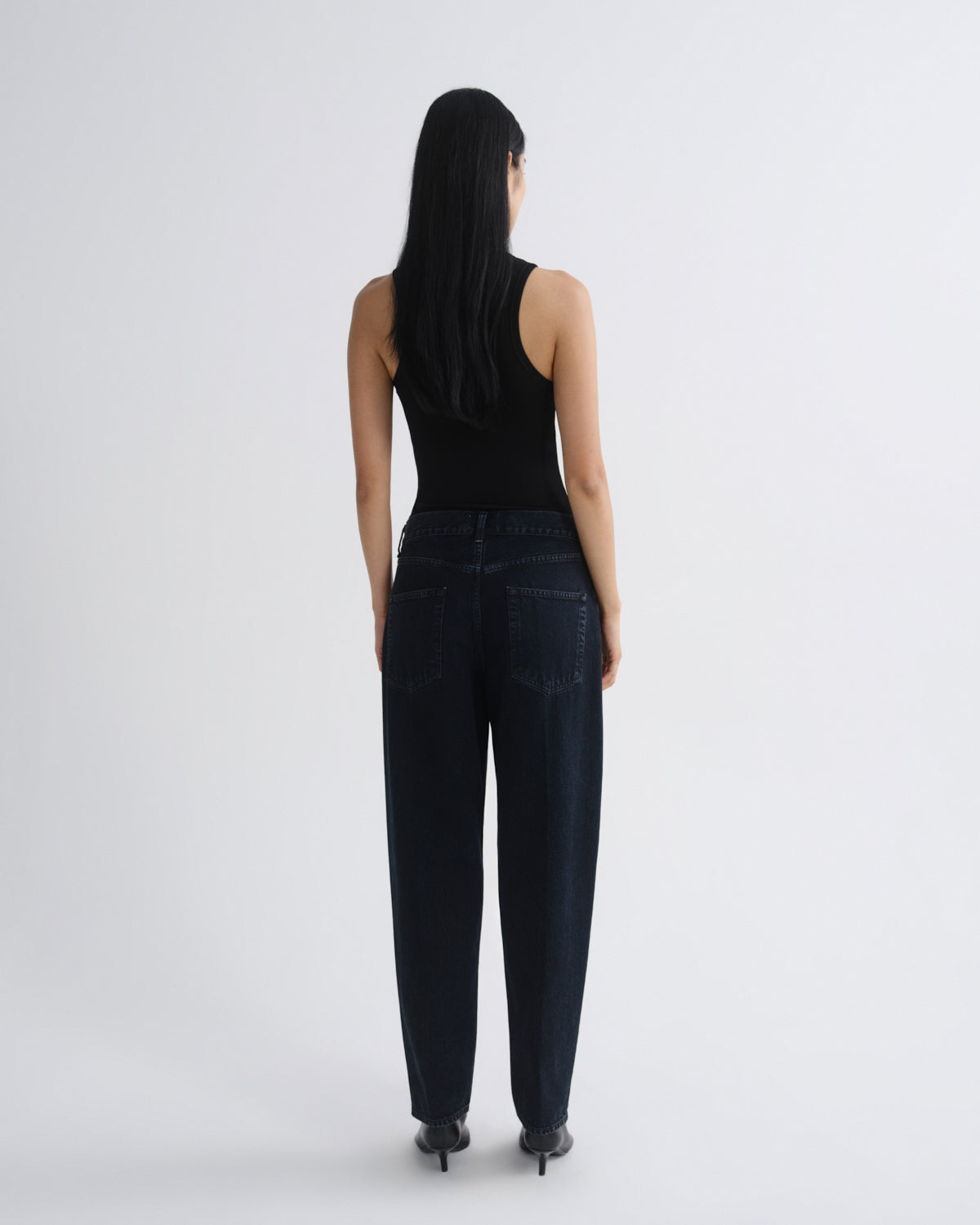 Person wearing black tank top and dark jeans on a white background