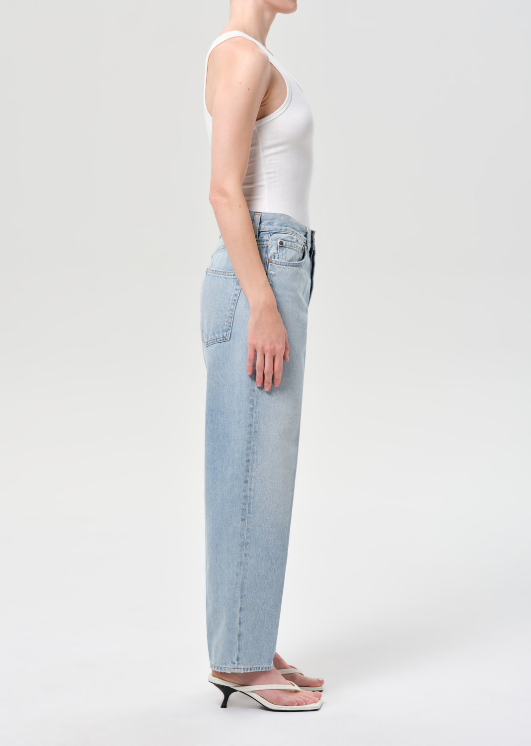 Person wearing light blue jeans and a white top on a plain background