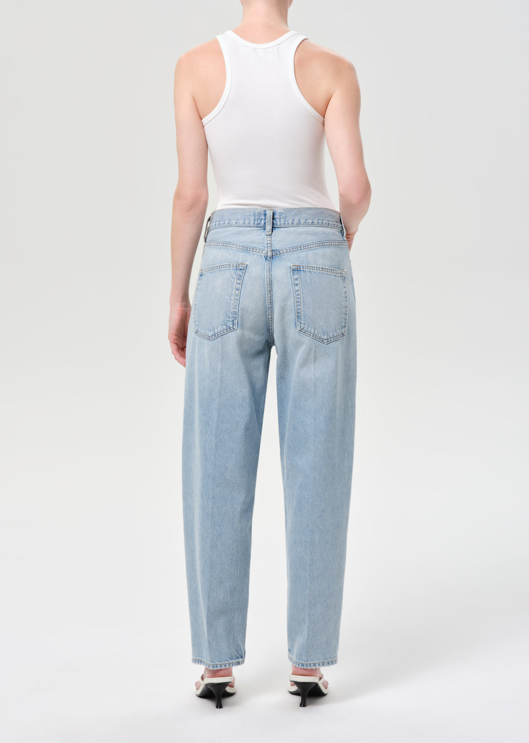 Person wearing light blue jeans and a white tank top on a white background
