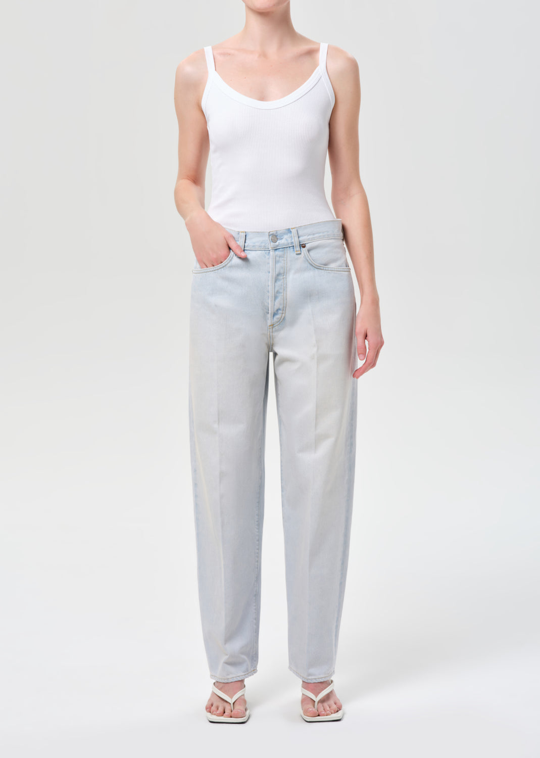 Person wearing a white tank top and light blue jeans on a white background