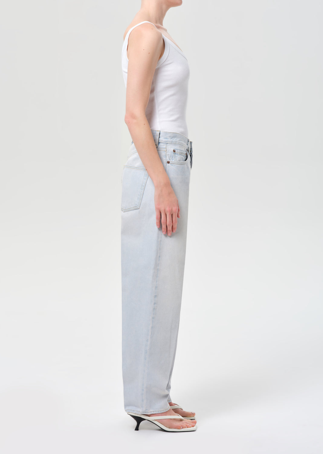 Person wearing light blue jeans and a white tank top on a white background