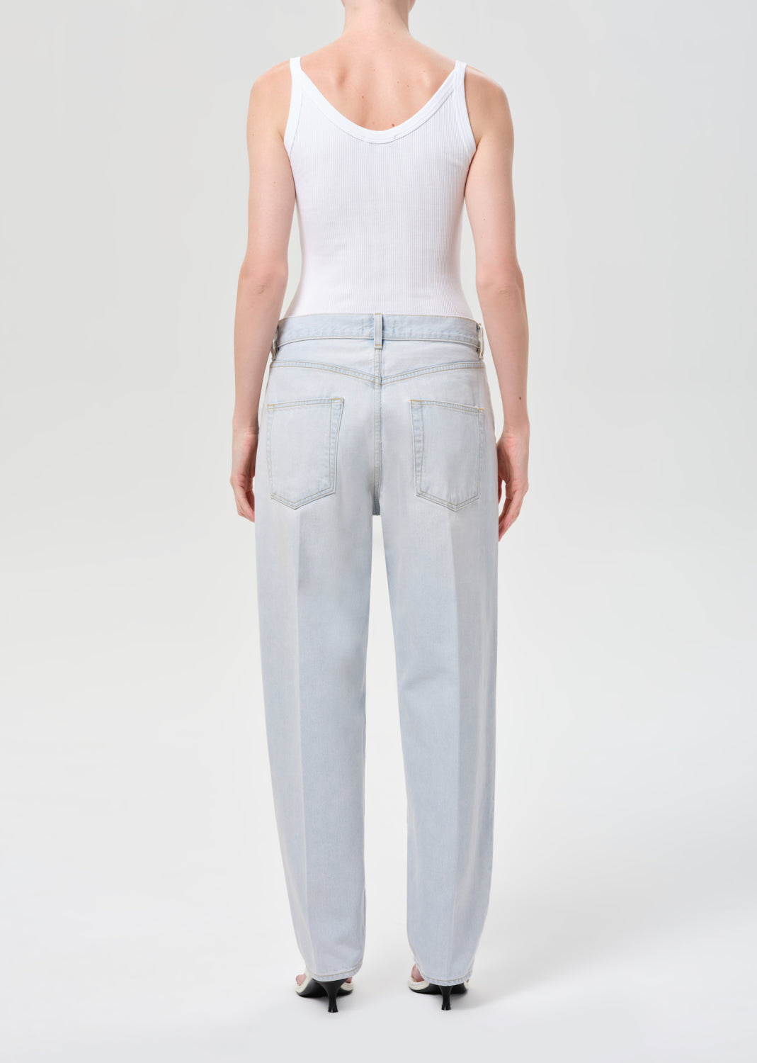 Person wearing light blue jeans and a white tank top on a white background