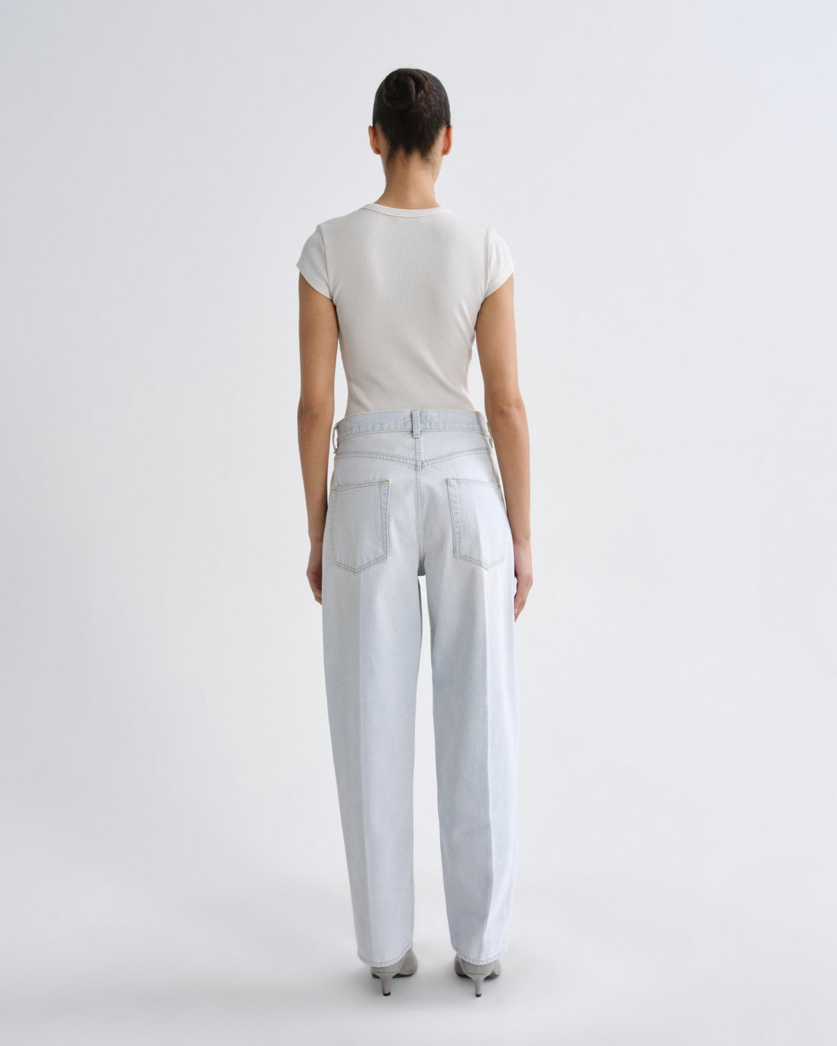 Person wearing light blue jeans and a white top on a plain background