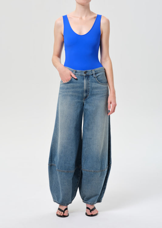 Person wearing a blue tank top and wide-leg jeans on a white background