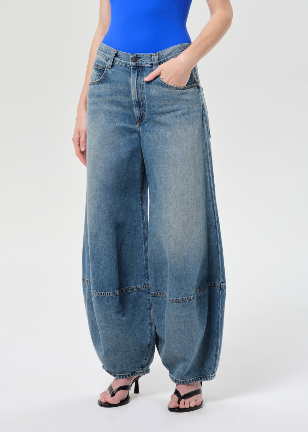 Person wearing blue wide-leg jeans and a blue top on a white background