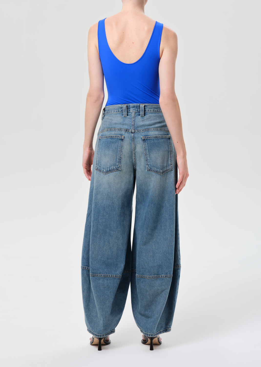 Person wearing blue tank top and wide-leg jeans on a white background
