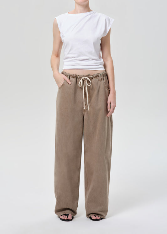 Person wearing a white sleeveless top and beige drawstring pants on a white background