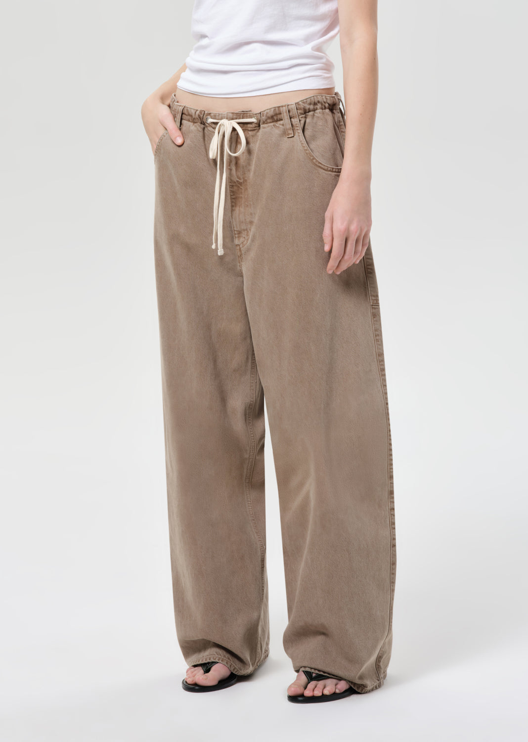 Person wearing beige wide-leg pants with a white top on a light gray background