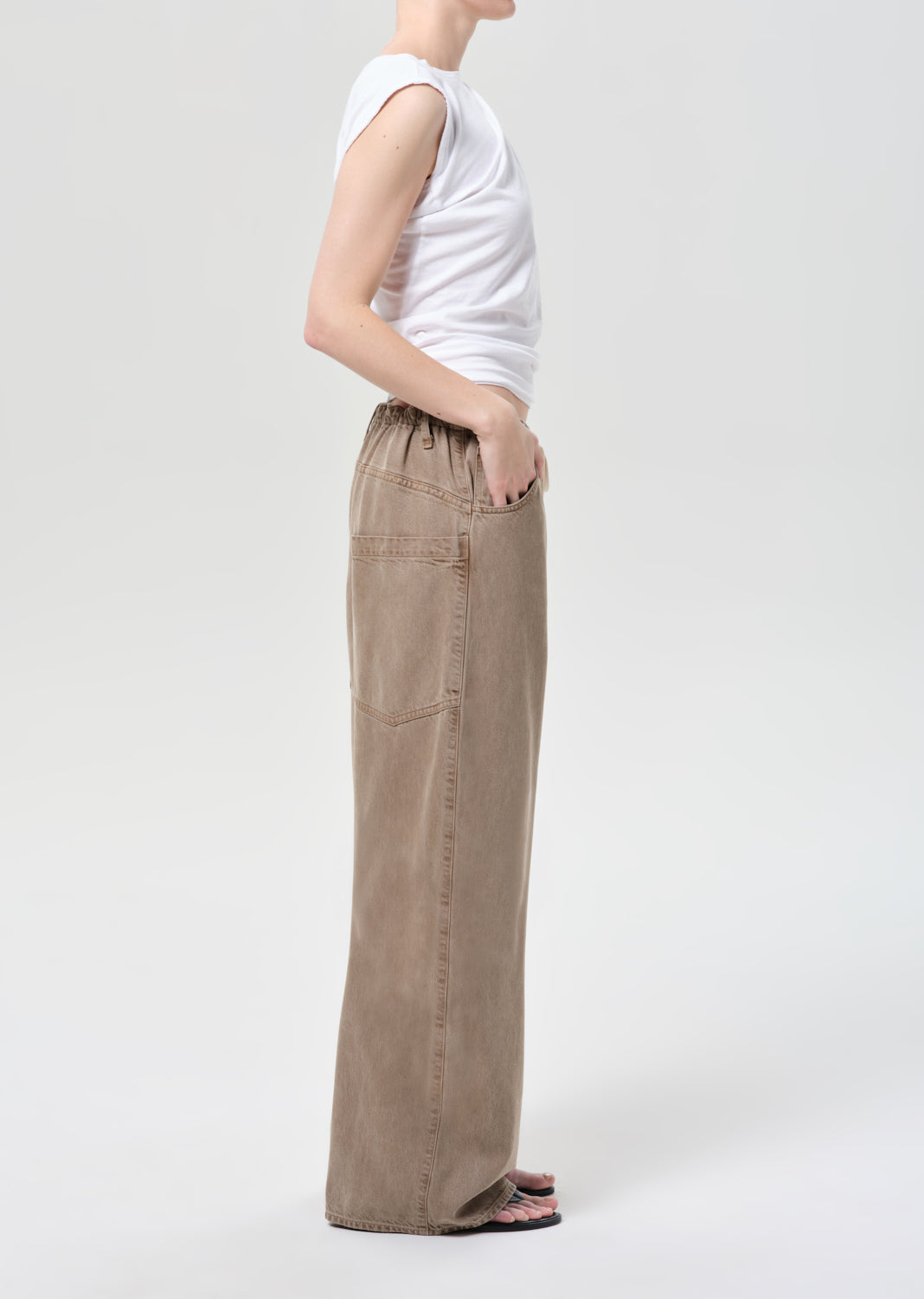 Person wearing beige wide-leg pants and a white top on a light gray background