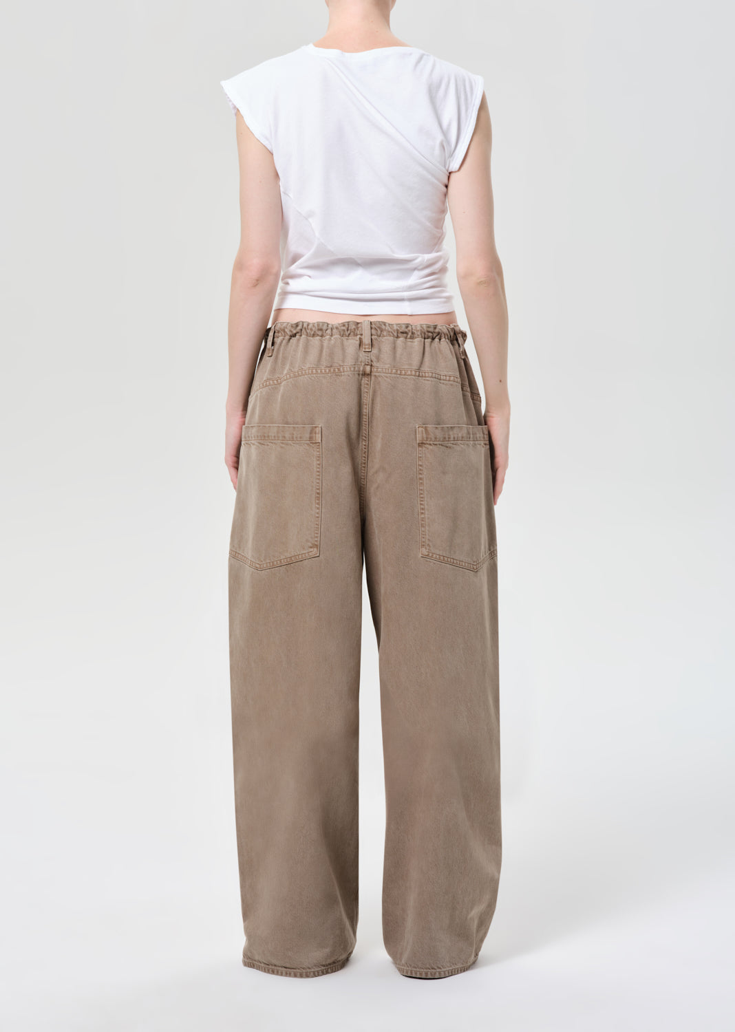 Person wearing beige wide-leg pants and a white top on a white background