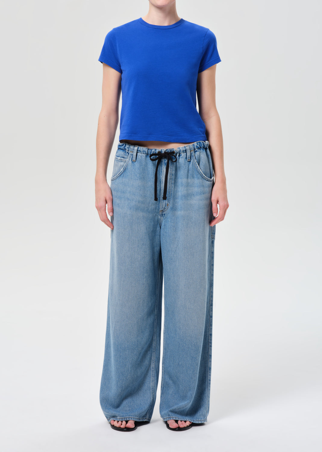 Person wearing a blue t-shirt and light blue wide-leg jeans on a white background