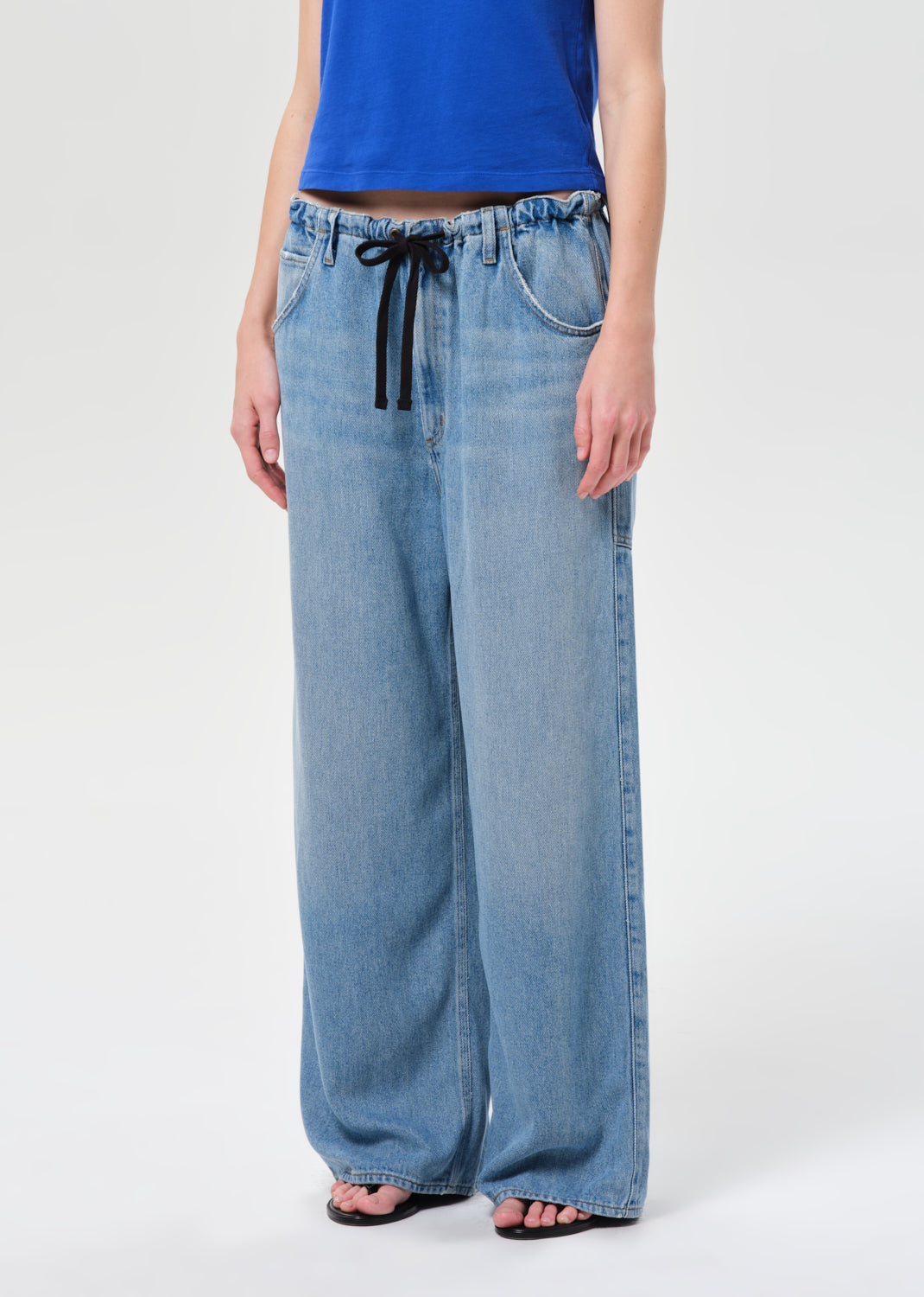 Person wearing light blue wide-leg jeans with a drawstring waist on a white background