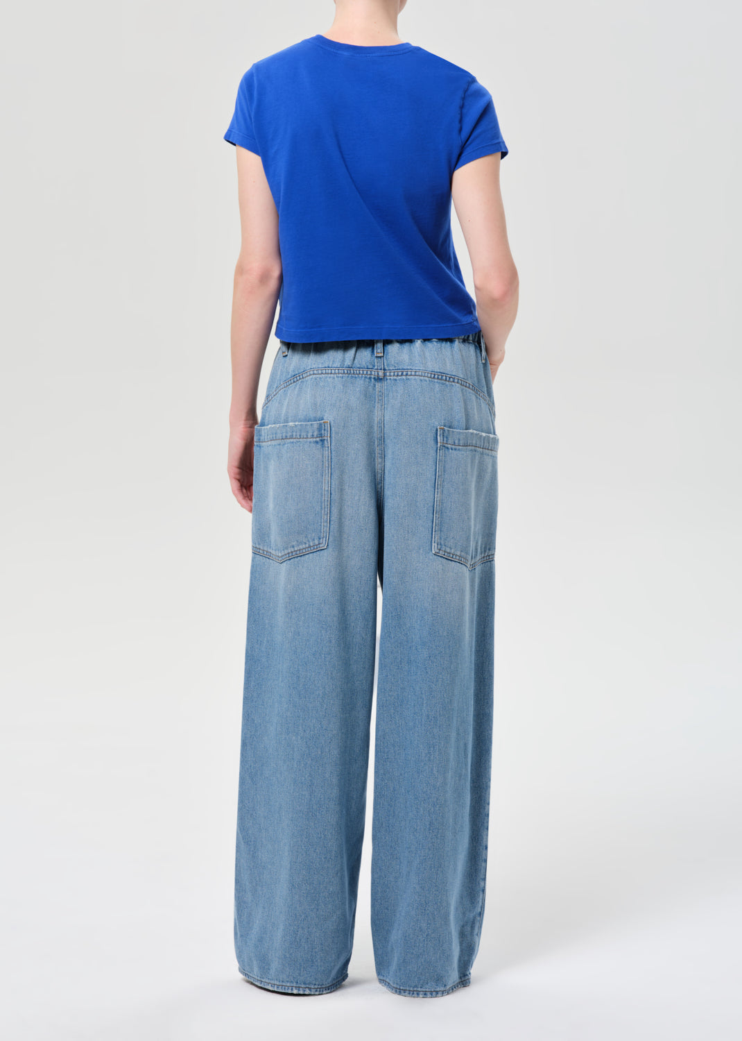 Person wearing a blue t-shirt and light blue wide-leg jeans on a white background