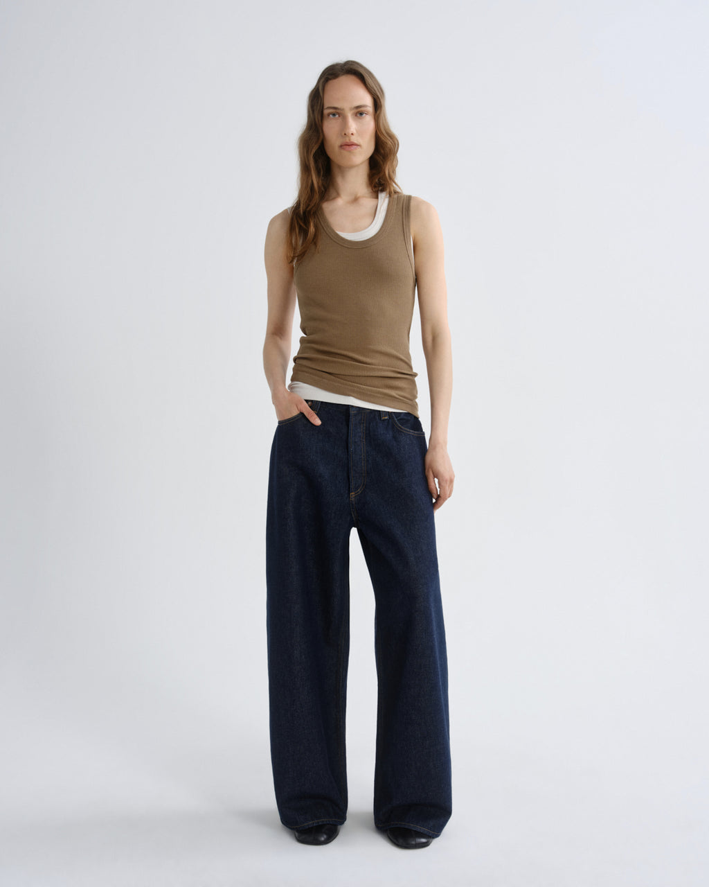 Woman wearing a brown tank top and dark blue wide-leg pants on a white background