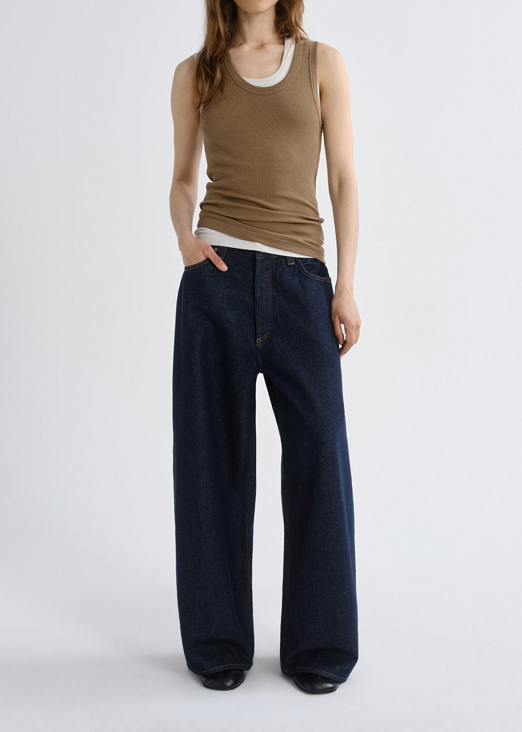 Person wearing a brown ribbed tank top with dark wash wide leg jeans on a grey background