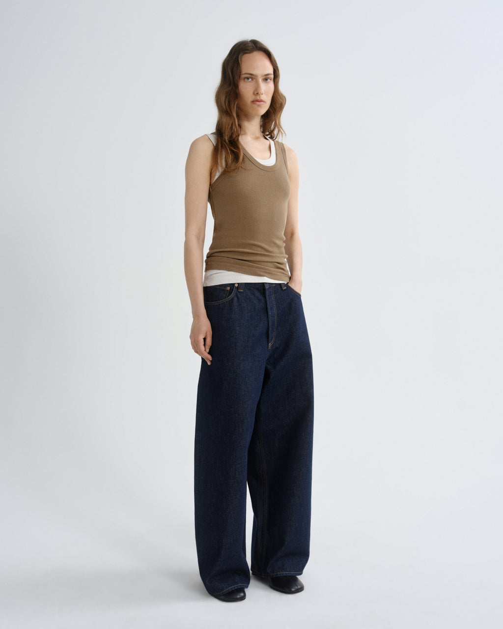 Woman wearing a brown tank top and dark blue wide-leg pants on a white background