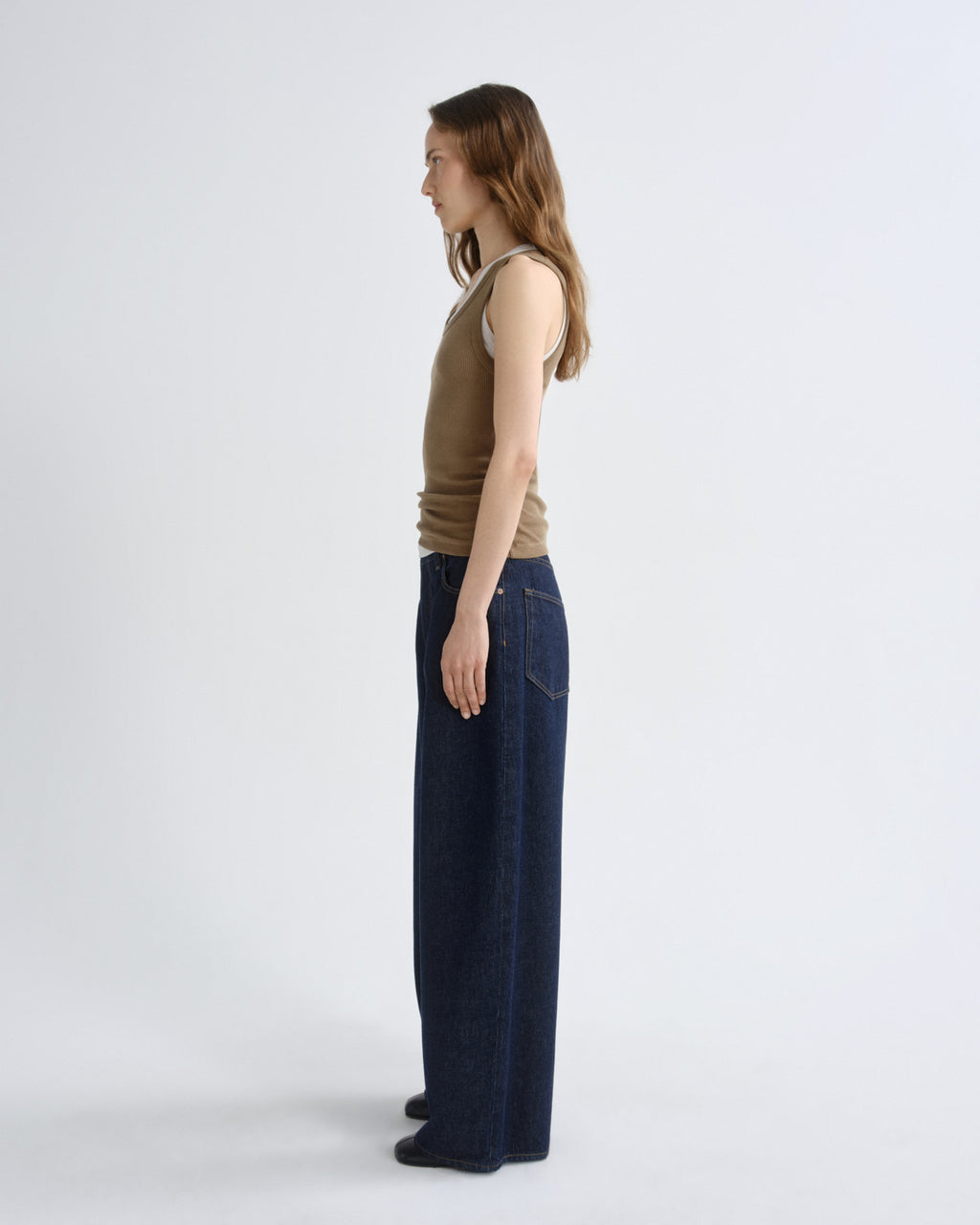 Woman wearing a brown sleeveless top and dark blue jeans on a white background