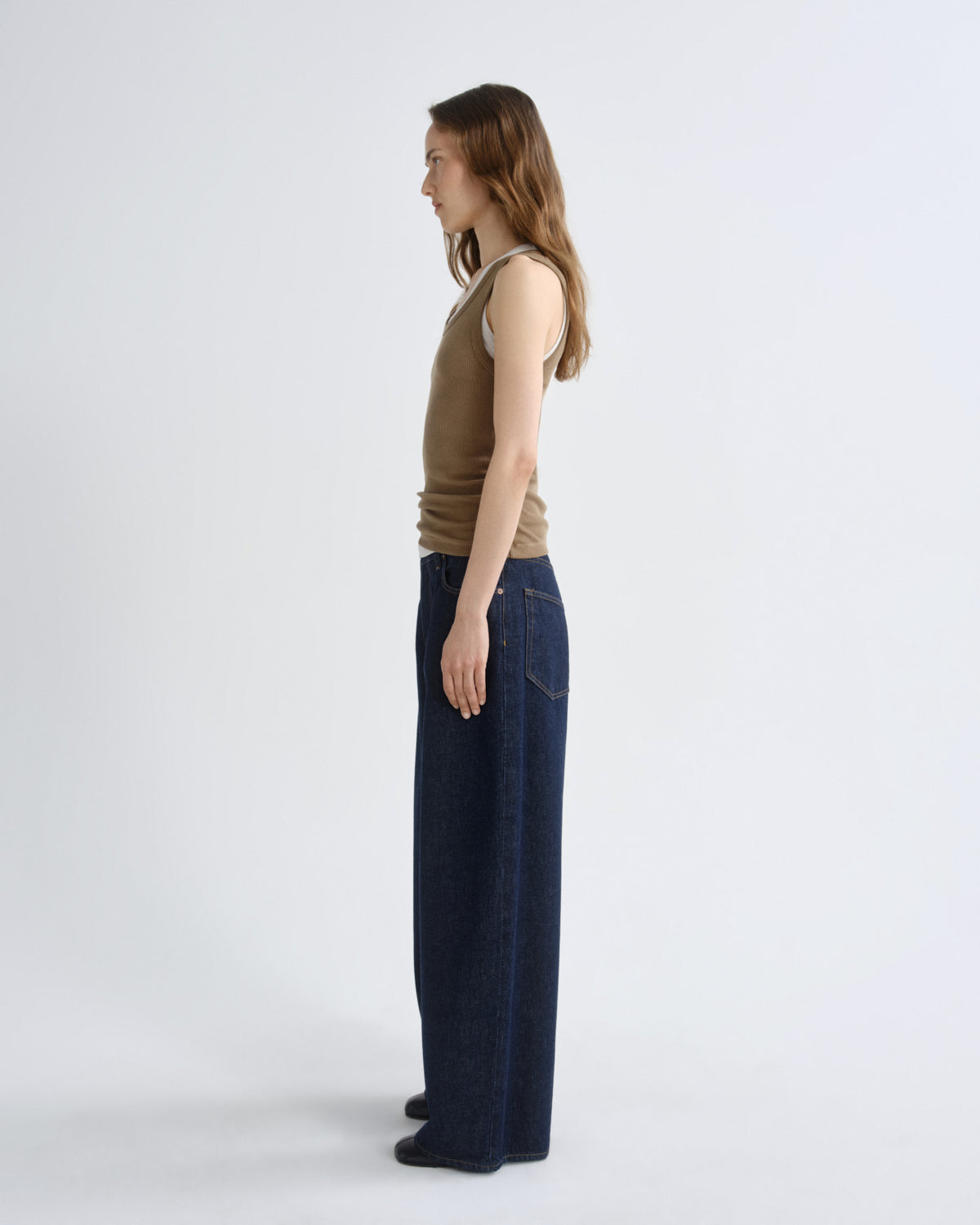 Woman wearing a brown sleeveless top and dark blue jeans on a white background