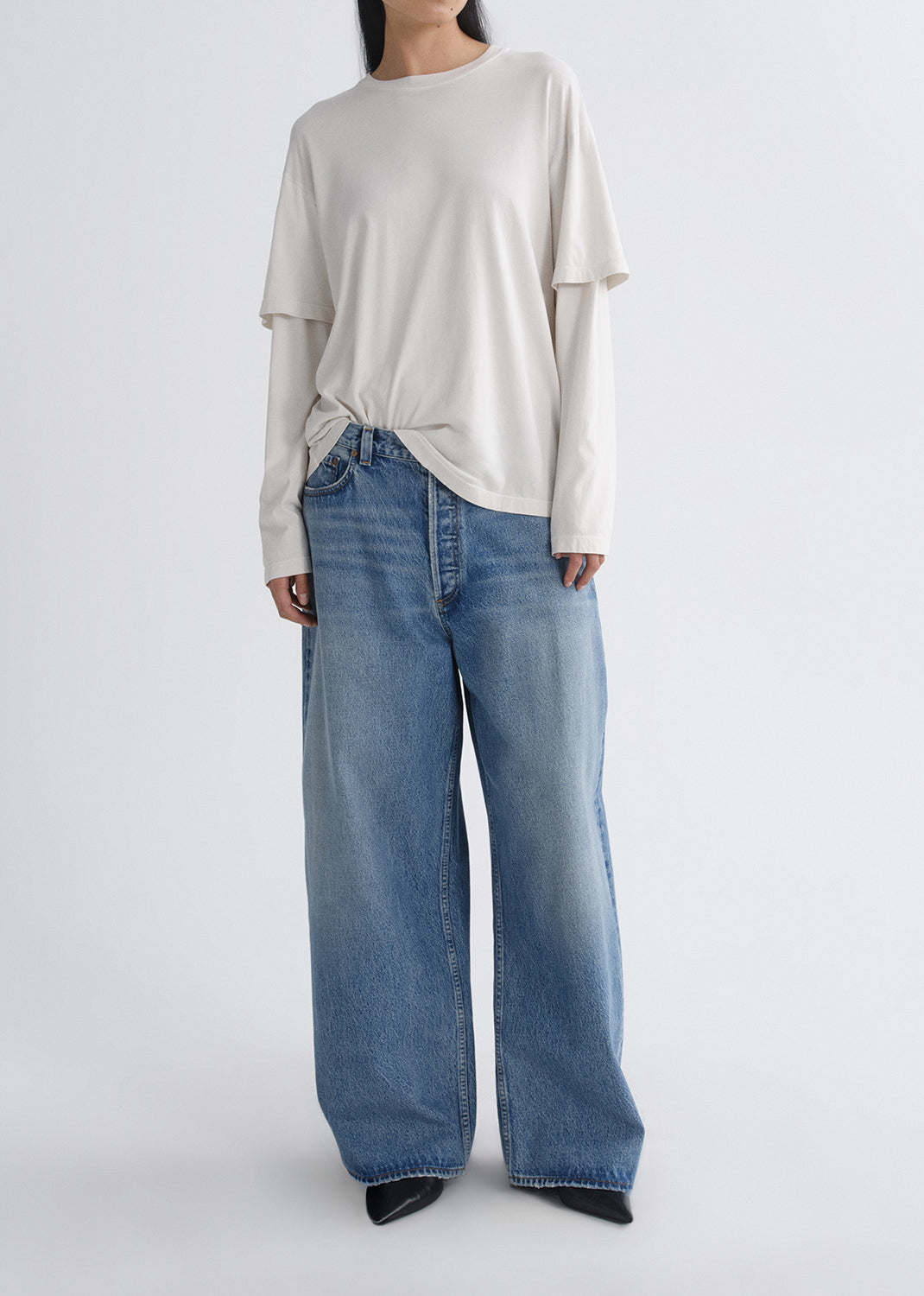 Person wearing a cream long sleeve tee with light wash wide leg jeans on a grey background
