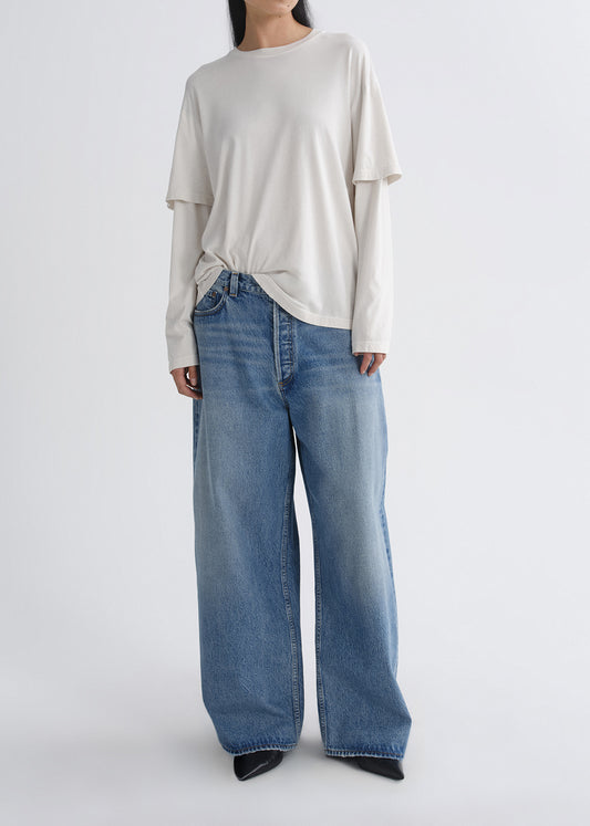 Person wearing a cream long sleeve tee with light wash wide leg jeans on a grey background