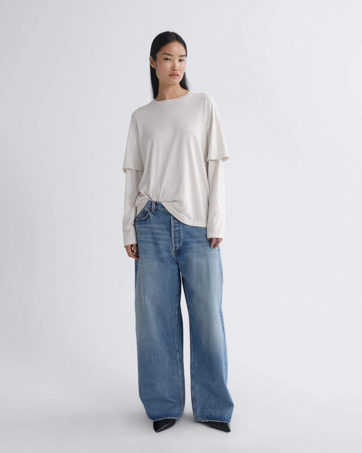 Person wearing a white top and blue jeans on a white background