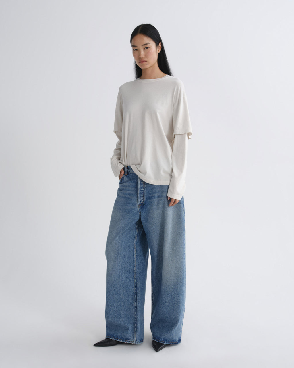 Person wearing a light gray sweater and blue jeans on a white background