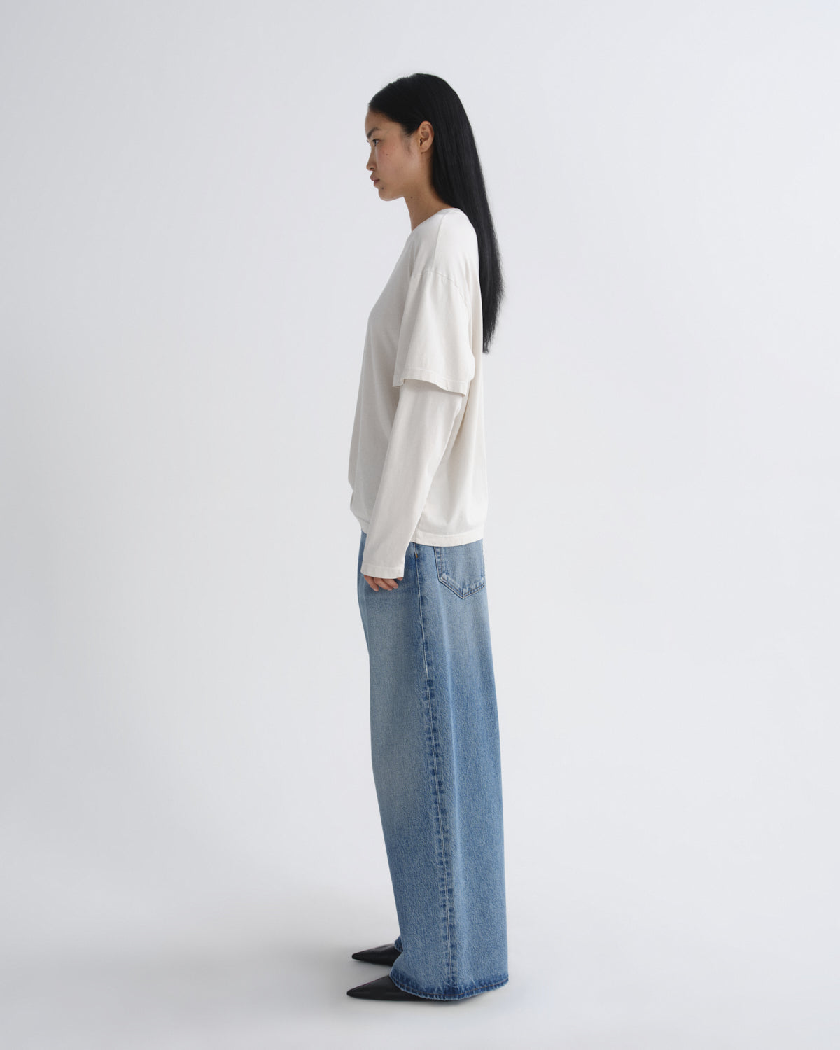 Person wearing a white top and blue jeans standing against a white background