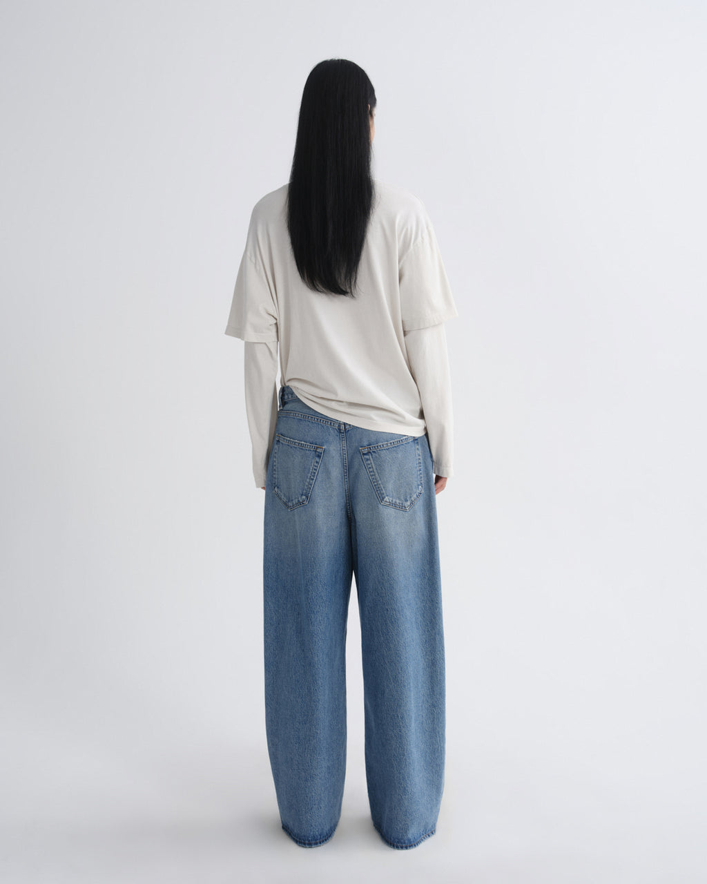Person wearing a light-colored top and blue jeans on a white background
