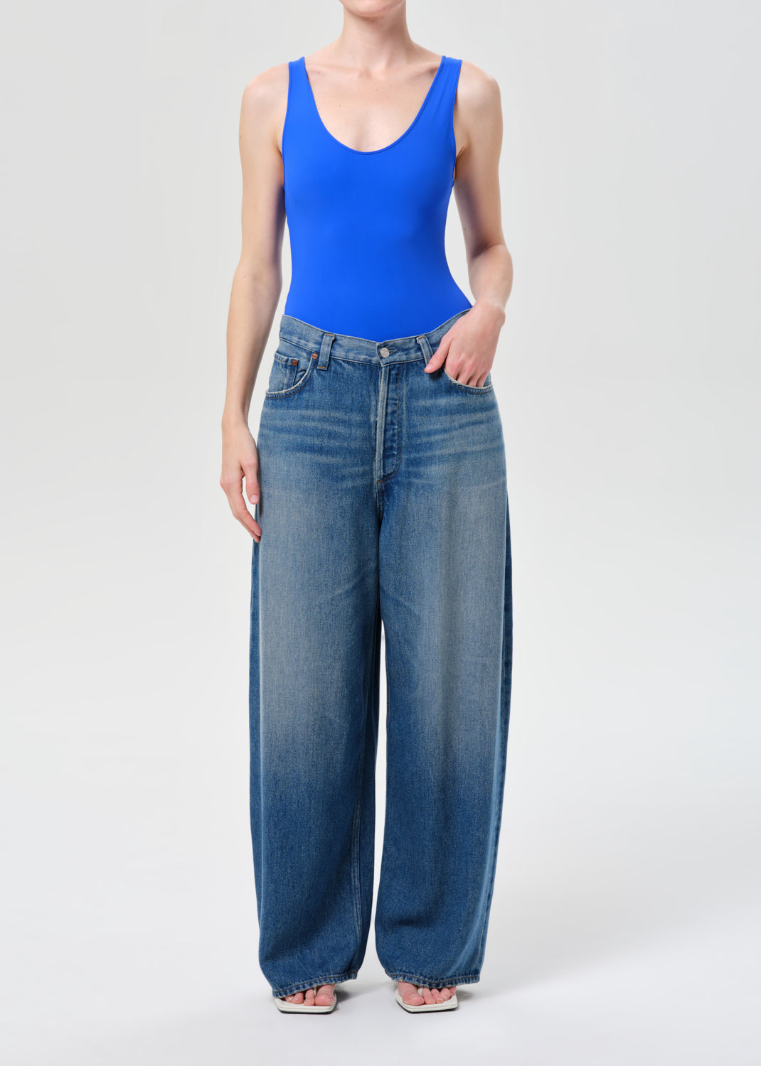 Person wearing a blue tank top and wide-leg jeans on a white background
