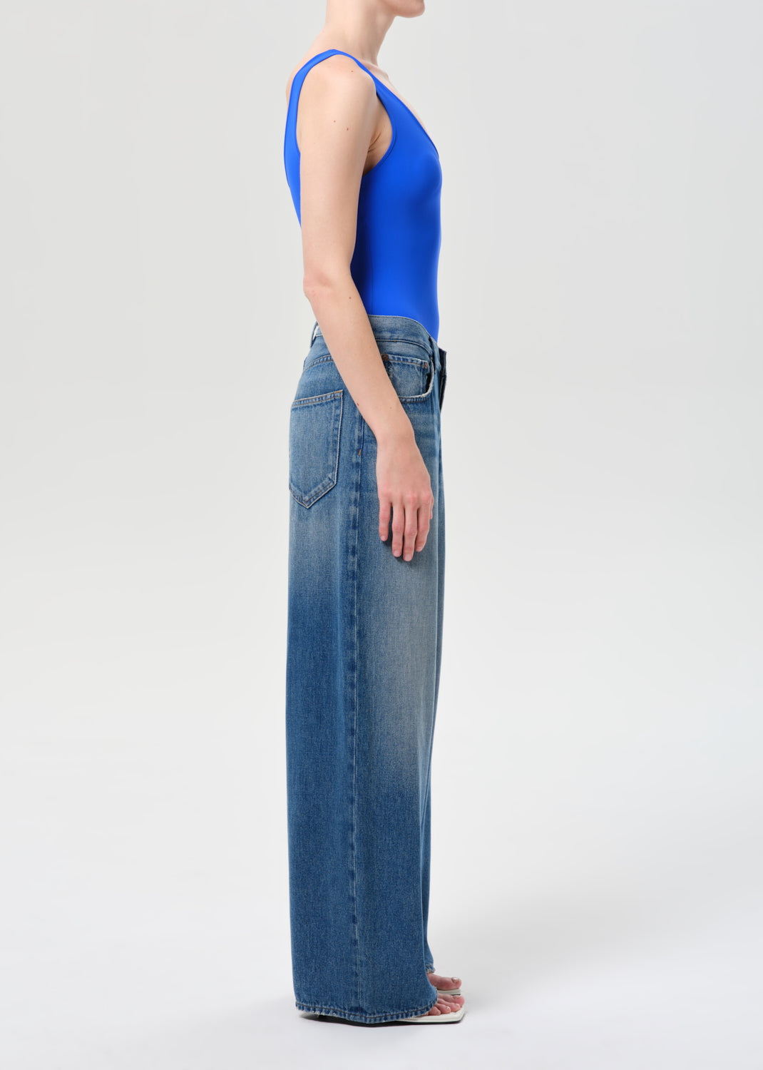 Person wearing a blue tank top and jeans on a white background