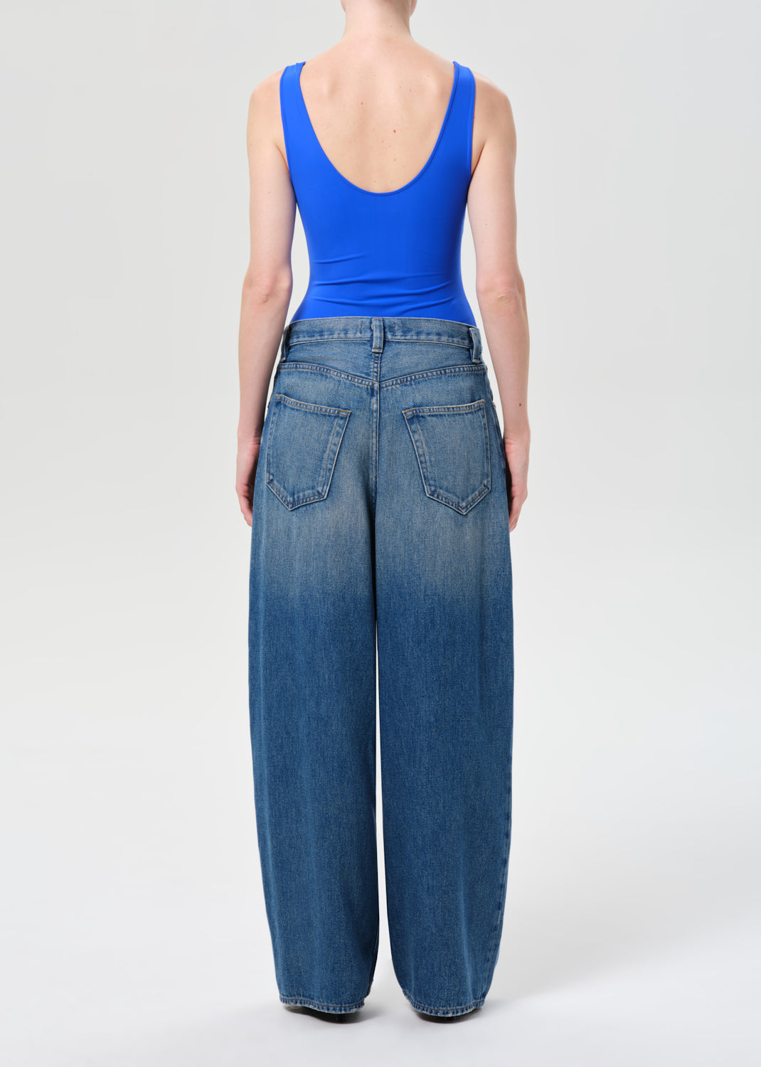 Person wearing a blue tank top and wide-leg jeans on a white background