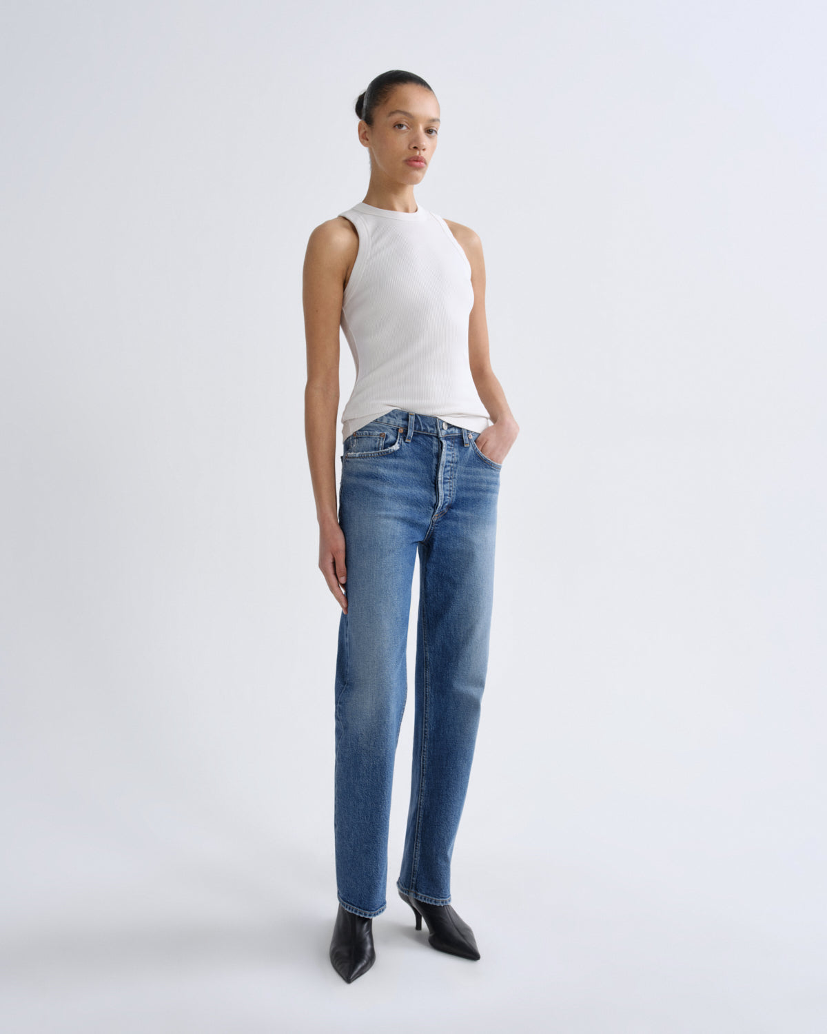 Woman wearing a white sleeveless top and blue jeans on a white background