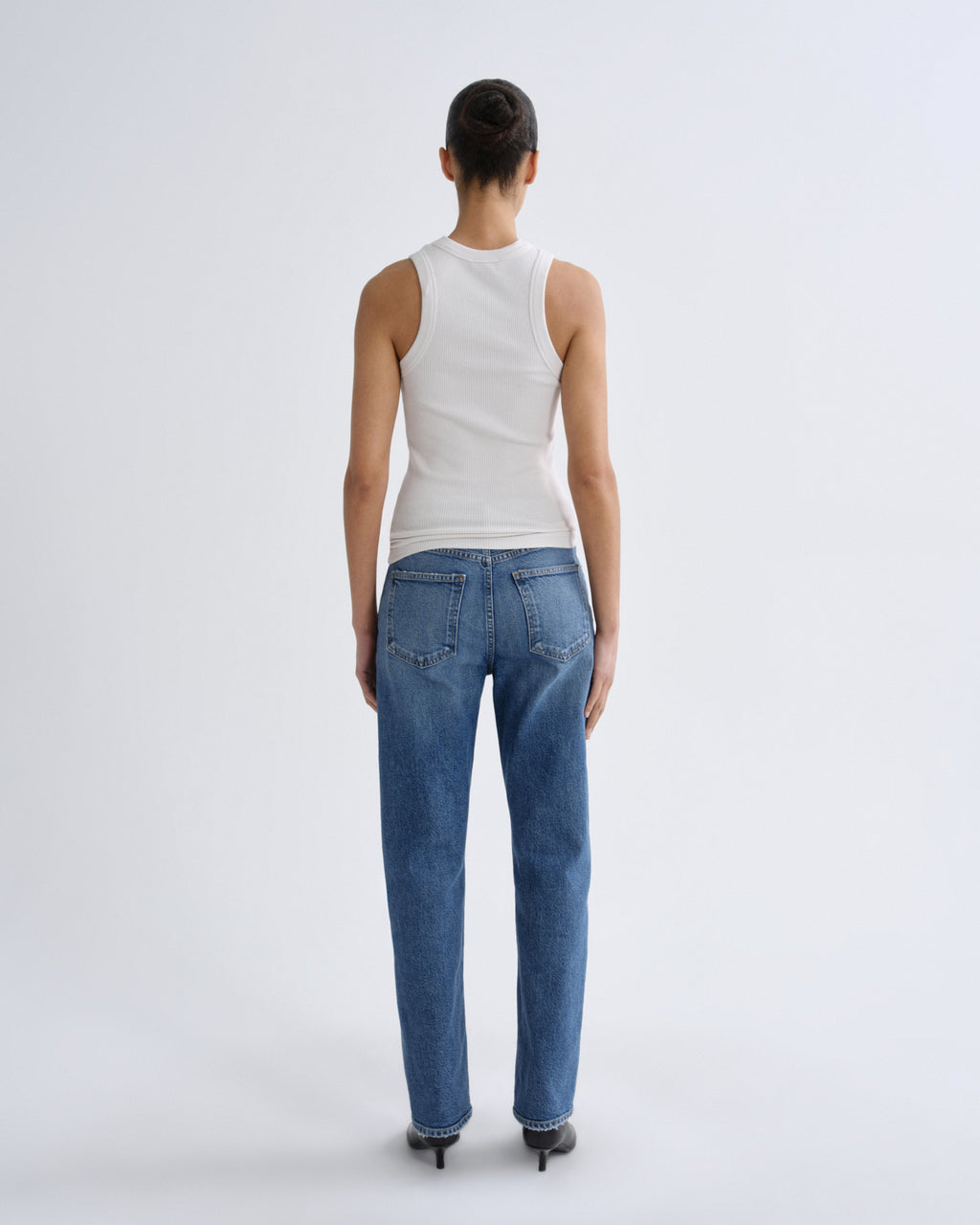 Person wearing blue jeans and a white tank top on a light gray background