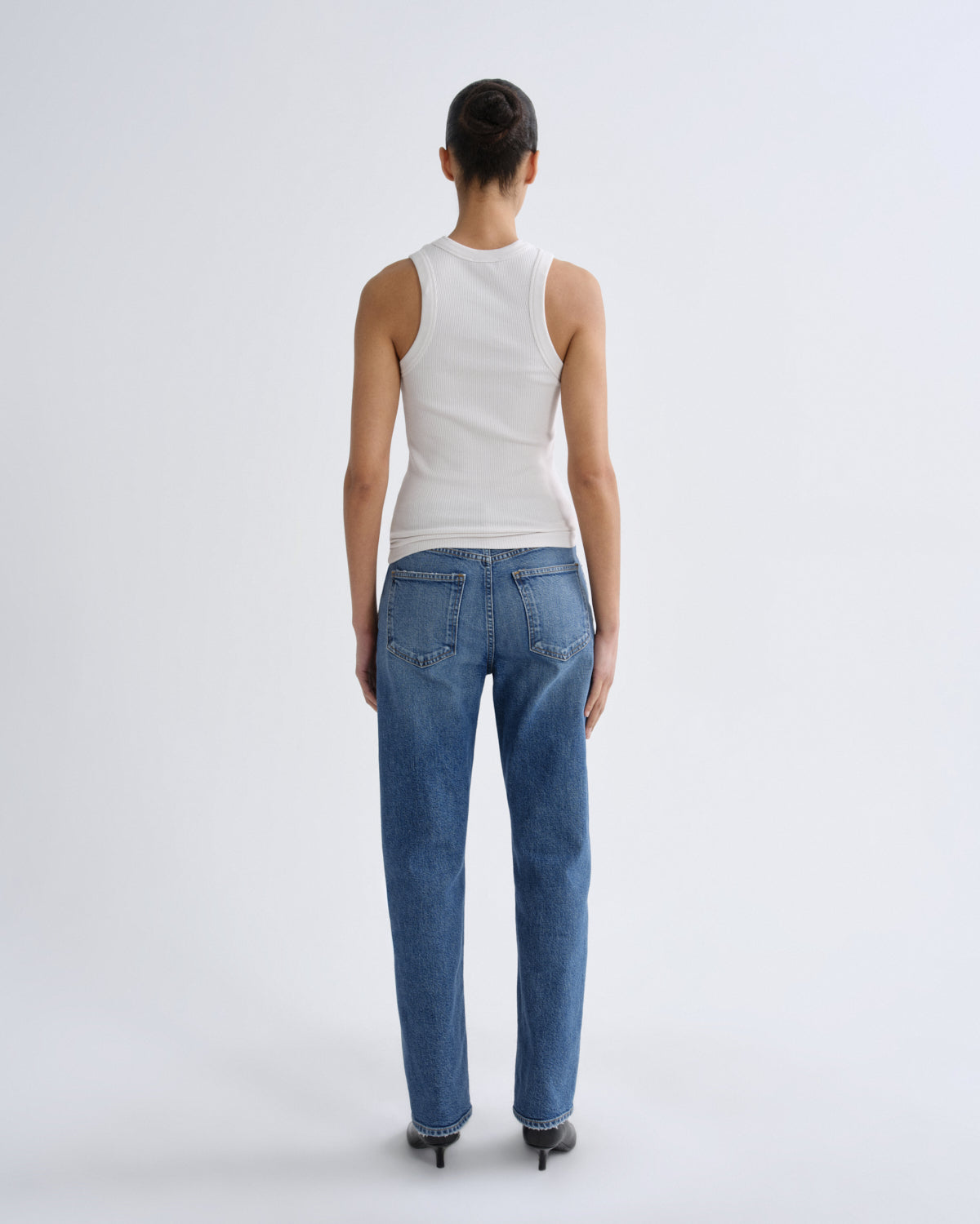 Person wearing blue jeans and a white tank top on a light gray background