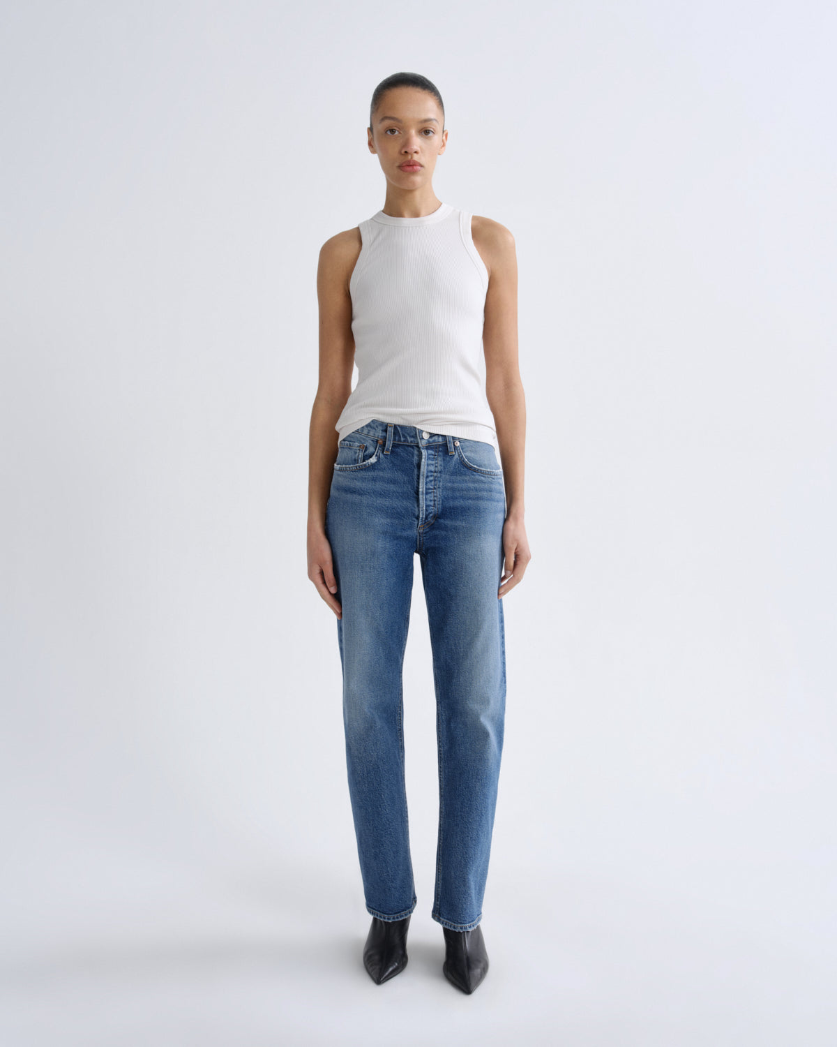 Person wearing a white sleeveless top and blue jeans on a white background