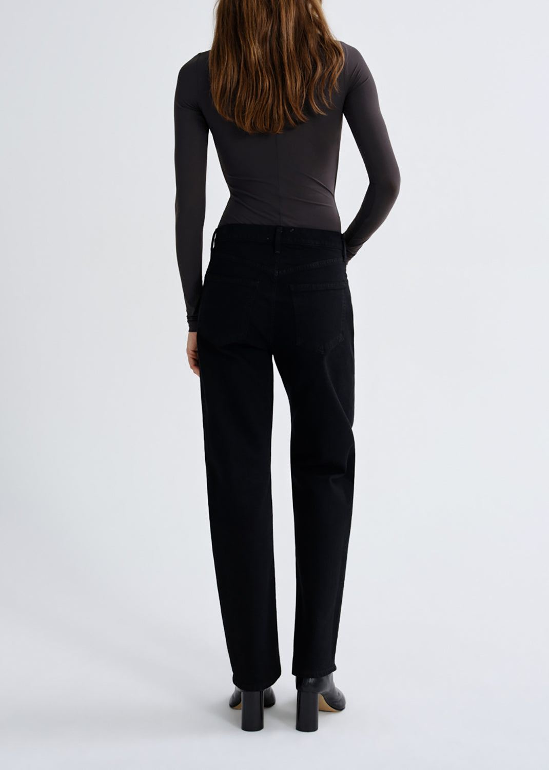 A woman shown from the back wearing a fitted black long-sleeve top and black straight-leg pants against a grey background.