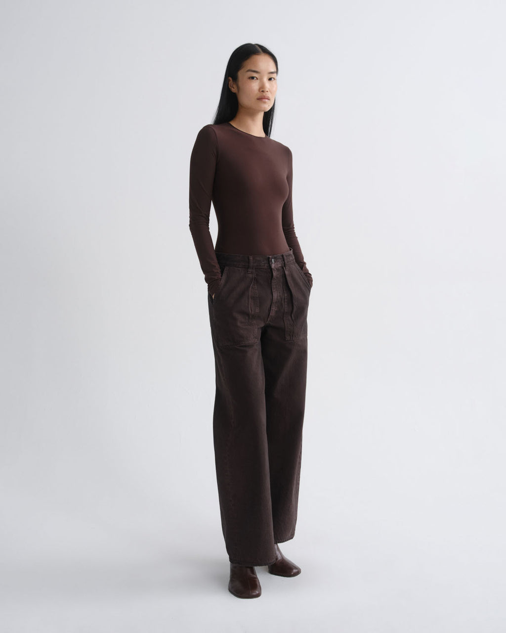 A model stands in profile wearing a dark brown long-sleeve knit top and matching dark brown wide-leg trousers against a plain light gray studio background.