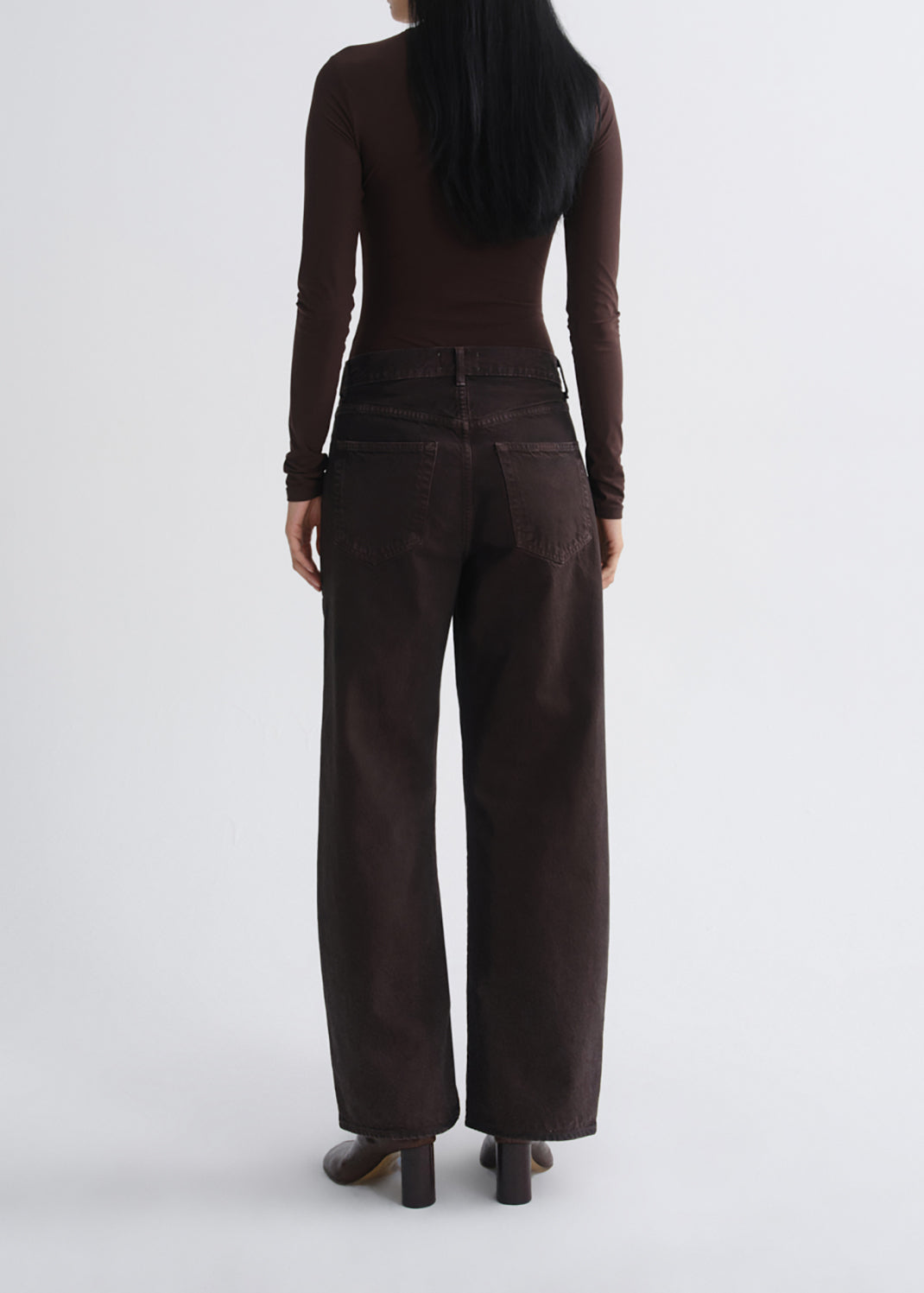 A model viewed from the back wearing a dark brown long-sleeve top and matching dark brown wide-leg trousers, paired with dark brown block-heel shoes, against a grey background.